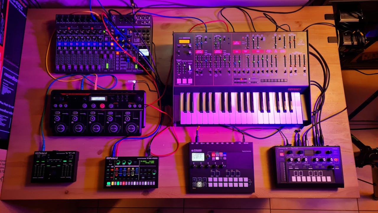 A diverse electronic music setup featuring synthesizers and mixers on a table with vibrant lighting.